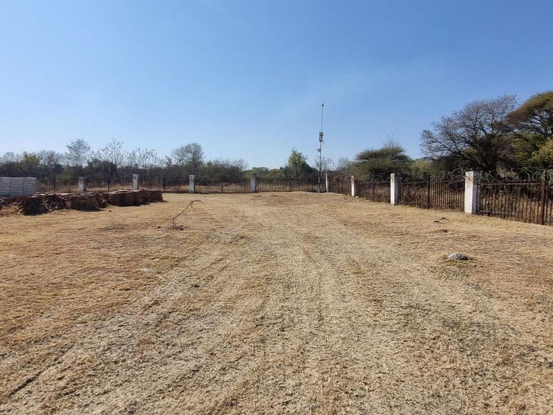 A vacant residential plot featuring perimeter fencing, a concrete boundary wall, and established security measures, ready for development.