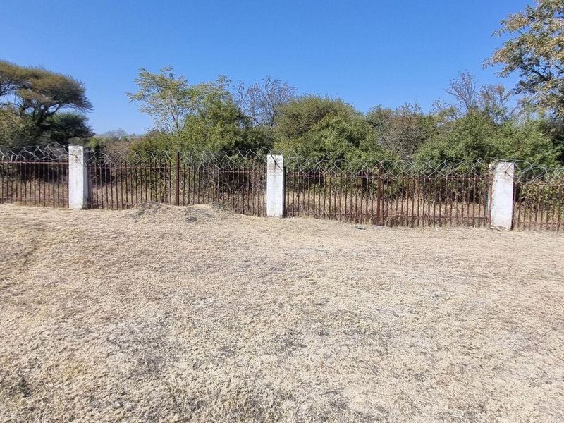 A view of the vacant residential land featuring a perimeter fence with concrete posts and rusted metal railing topped with razor wire.