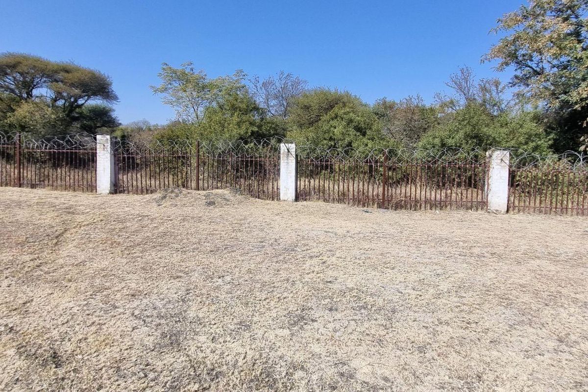 A view of the vacant residential land featuring a perimeter fence with concrete posts and rusted metal railing topped with razor wire.