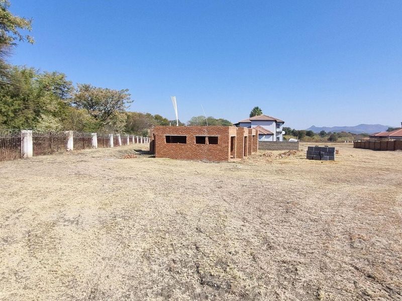A vacant residential plot featuring an incomplete brick masonry structure and perimeter fencing, offering a blank canvas for development.