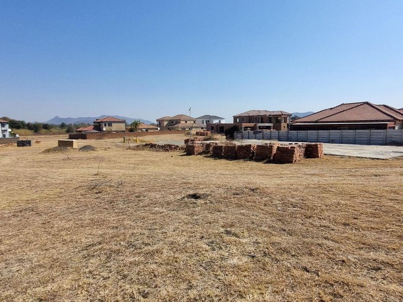 A vacant residential plot featuring a concrete slab, boundary wall, and piles of construction bricks in a developing estate setting.