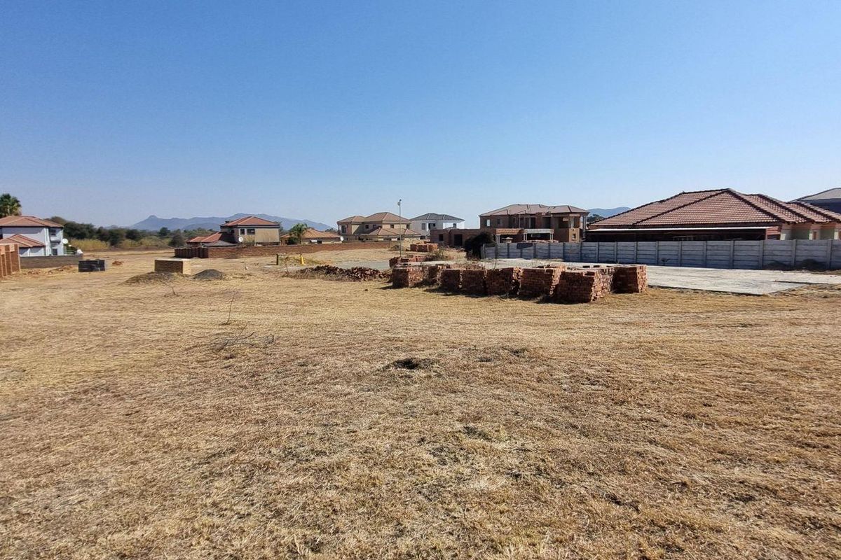 A vacant residential plot featuring a concrete slab, boundary wall, and piles of construction bricks in a developing estate setting.