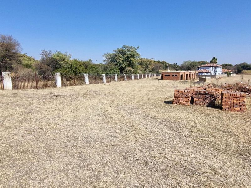 A view of a vacant residential plot featuring perimeter fencing with concrete posts and razor wire, set within a developed estate environment.