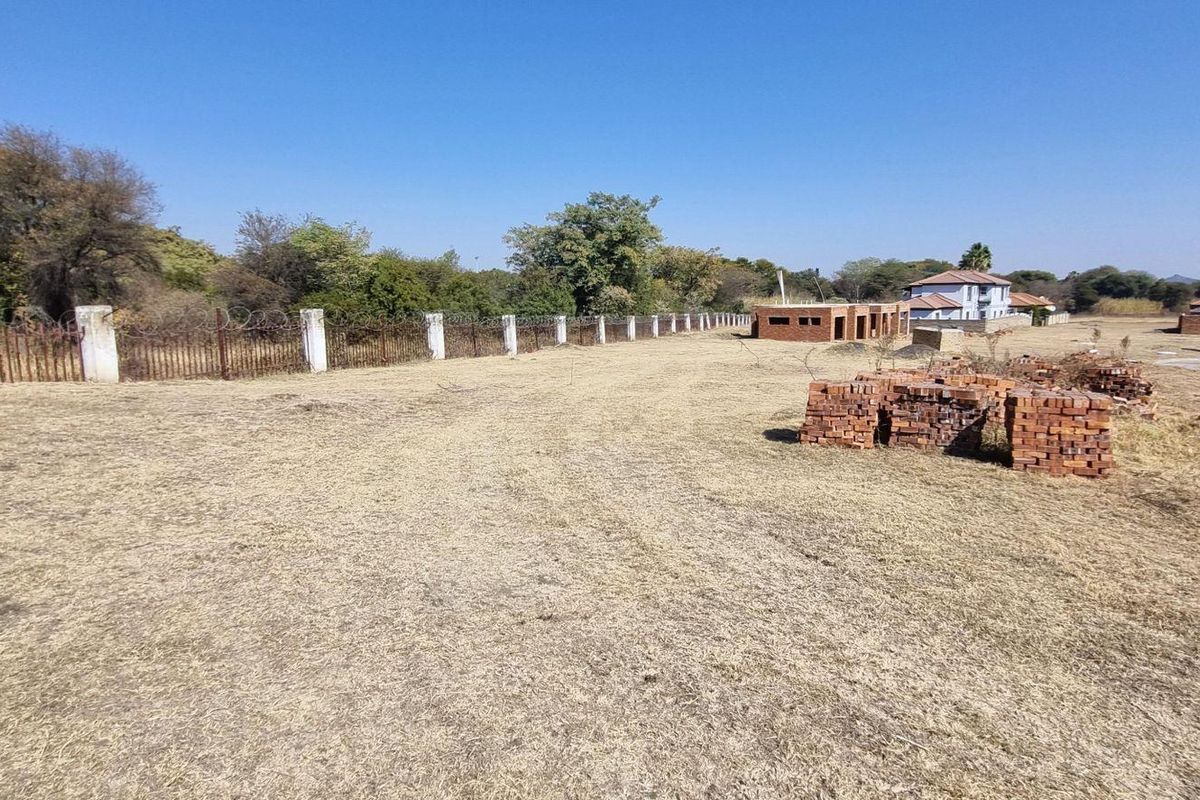 A view of a vacant residential plot featuring perimeter fencing with concrete posts and razor wire, set within a developed estate environment.