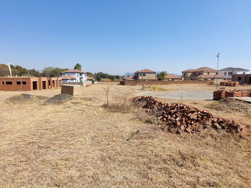 A wide-angle view of a vacant residential plot featuring construction materials, a concrete slab, and surrounding boundary walls in a developing estate.