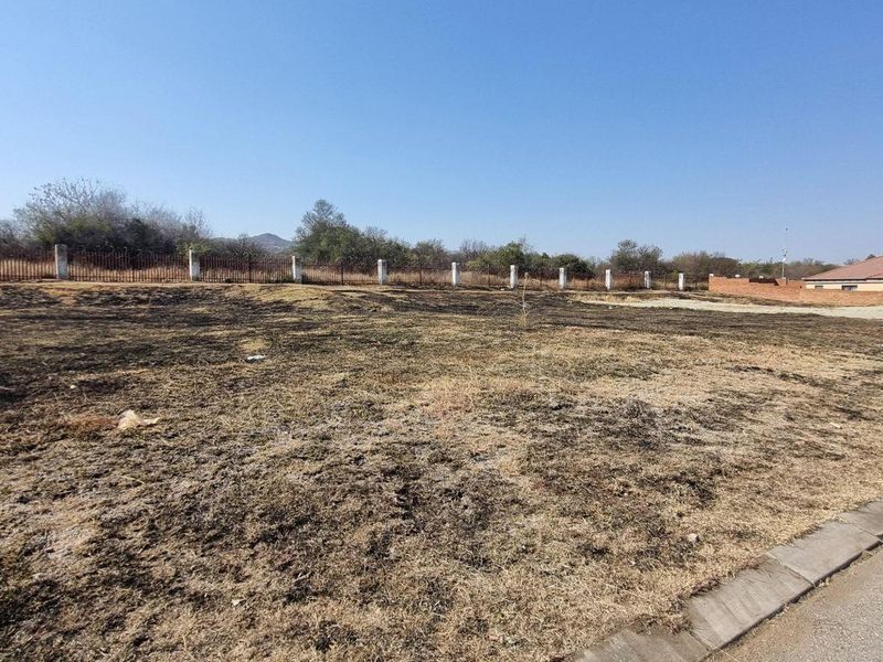 A vacant residential plot featuring a perimeter fence and paved curb, currently showing signs of scorched vegetation across the land.