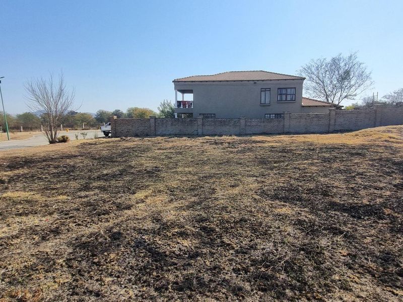 A vacant residential plot featuring a brick boundary wall, street access, and scorched ground, situated in a suburban neighborhood setting.
