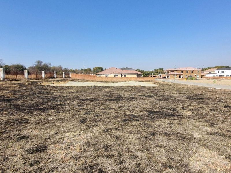 A vacant residential plot featuring perimeter fencing and direct access to a paved road in a developing neighborhood.