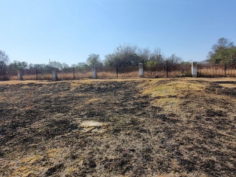 A view of a vacant residential plot featuring perimeter fencing and concrete pillars, with signs of recent vegetation clearing or fire damage on the ground.