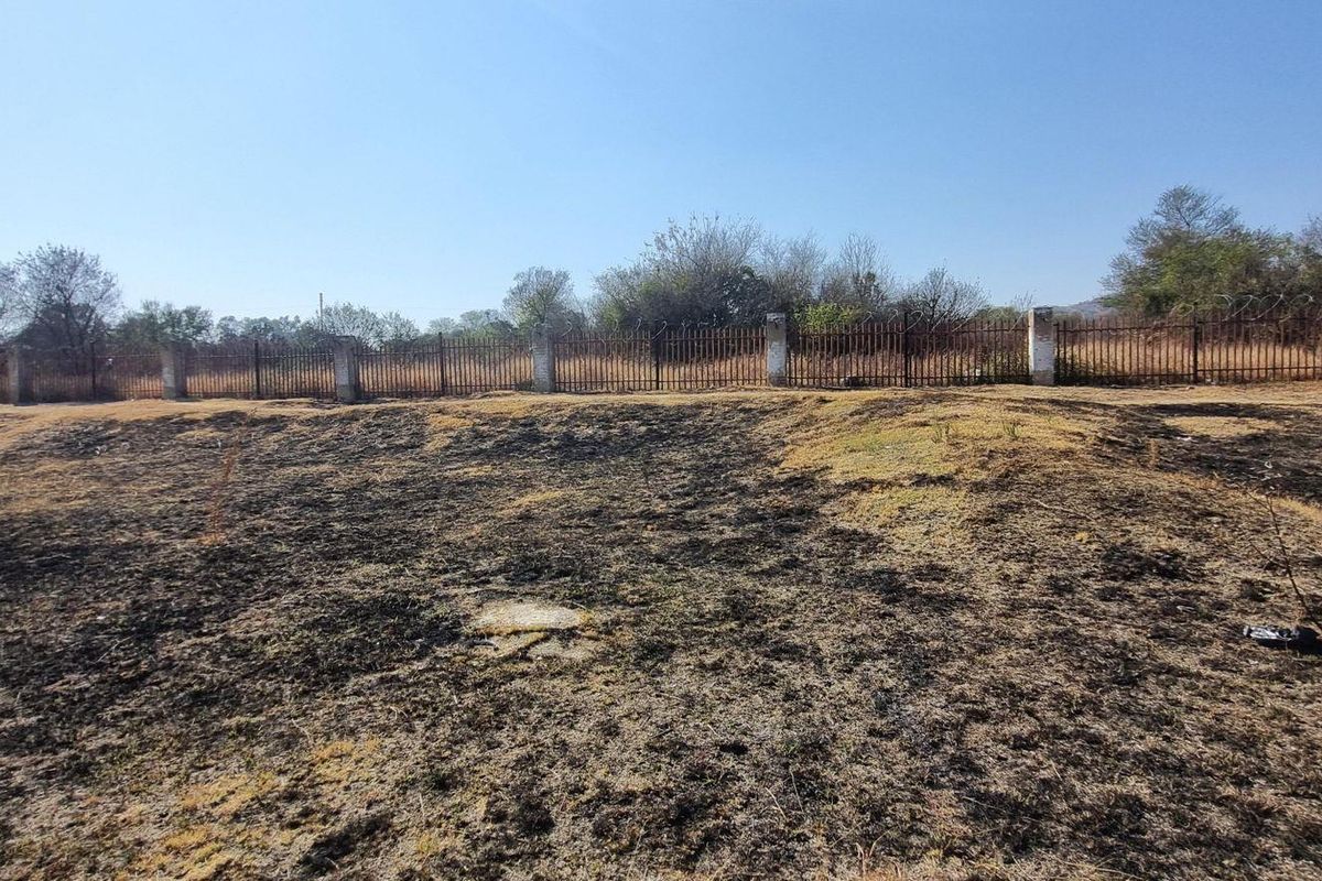 A view of a vacant residential plot featuring perimeter fencing and concrete pillars, with signs of recent vegetation clearing or fire damage on the ground.