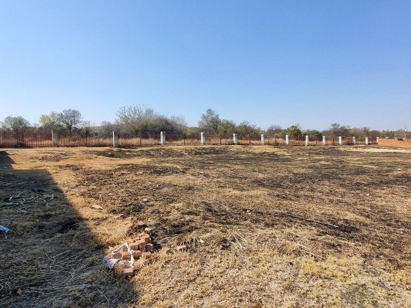 A vacant residential plot featuring a perimeter brick wall and metal fencing, with signs of recent ground clearing or fire damage.