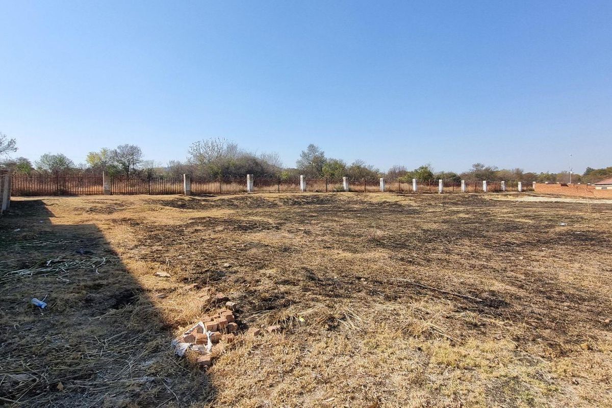 A vacant residential plot featuring a perimeter brick wall and metal fencing, with signs of recent ground clearing or fire damage.