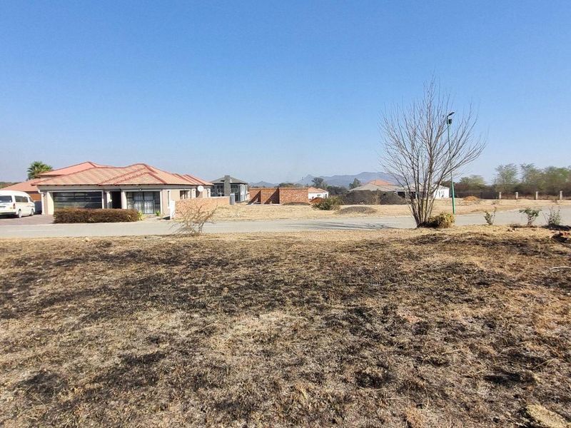 A vacant residential plot featuring dry, unmaintained ground cover and a partial brick boundary wall, situated in a developed suburban street.