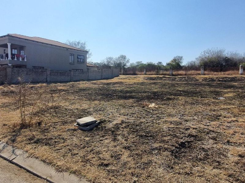 A vacant residential plot featuring a perimeter brick wall and metal fencing, situated along a paved street in a developed neighborhood.