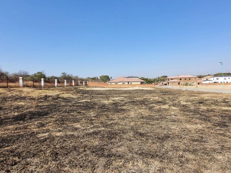 A vacant residential plot featuring perimeter fencing and direct access to a paved road, situated in a developed neighborhood.