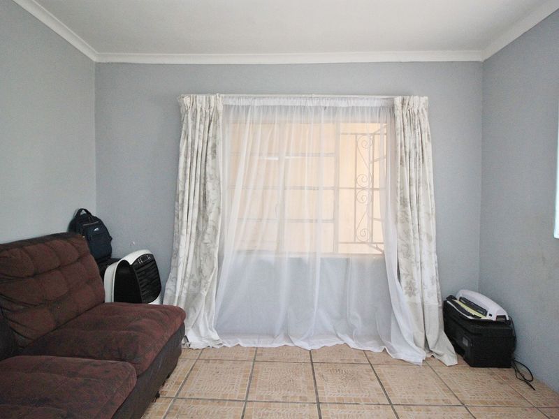 A simple bedroom featuring tiled flooring and a window fitted with a security gate.
