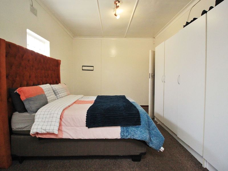 A functional bedroom featuring built-in white cupboards, neutral wall finishes, and a ceiling light fixture.