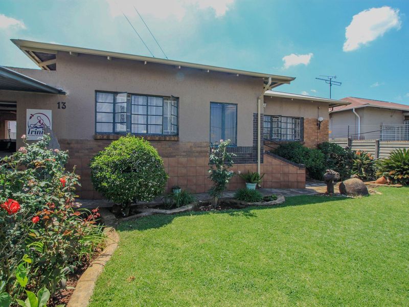 Front elevation of a single-story house featuring a tiled facade base, steel-framed windows, and a well-maintained front garden with a carport.