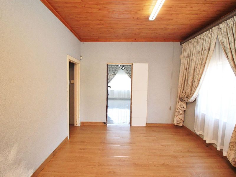 An empty living room featuring timber ceiling panels, laminate flooring, and a doorway leading to an adjacent room.