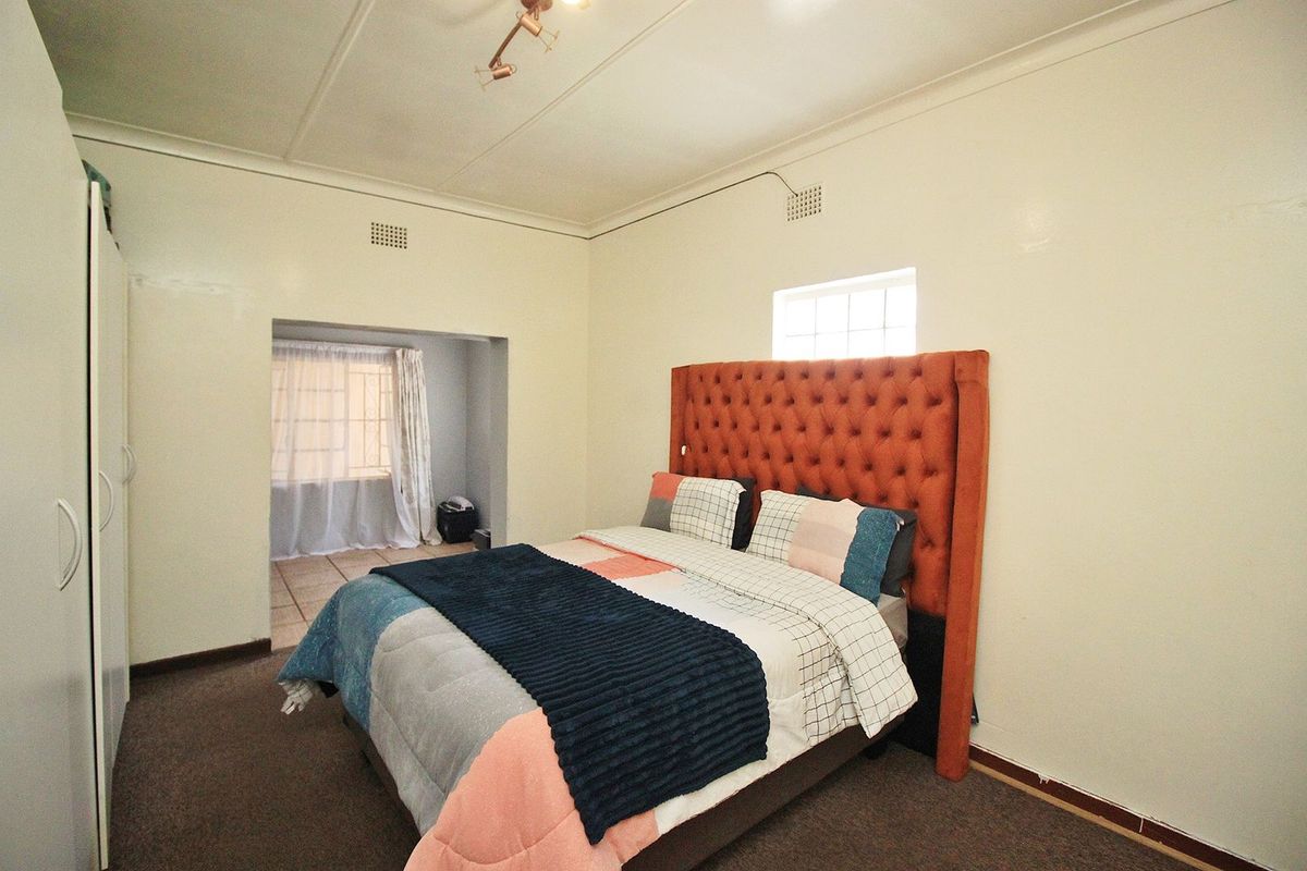 Spacious bedroom featuring a built-in wardrobe, high ceilings with ventilation, and an adjoining alcove area with natural light.
