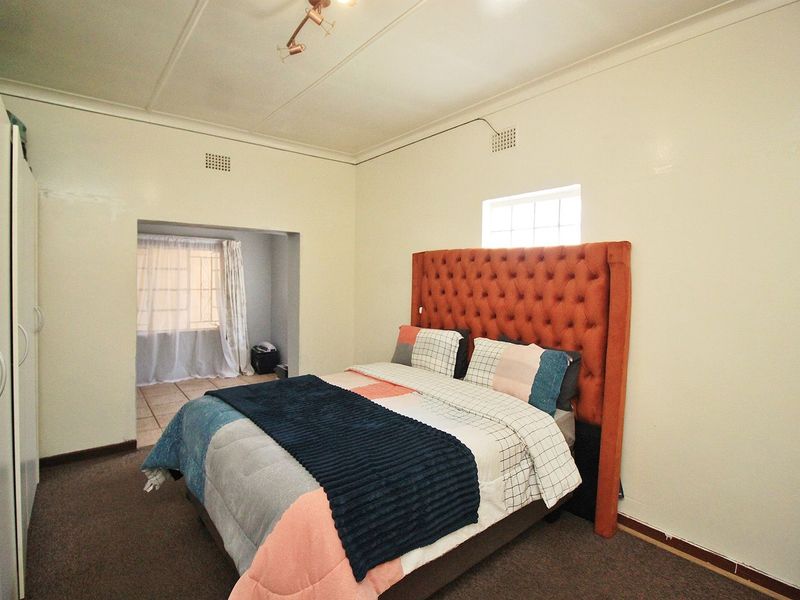 Spacious bedroom featuring a built-in wardrobe, high ceilings with ventilation, and an adjoining alcove area with natural light.