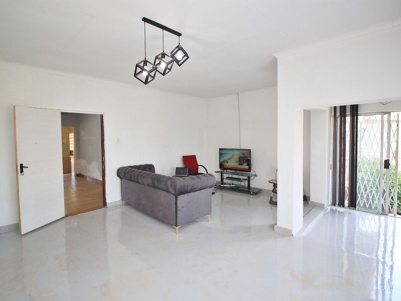 A bright living room featuring tiled flooring, modern pendant lighting, and a sliding glass door leading to the exterior.