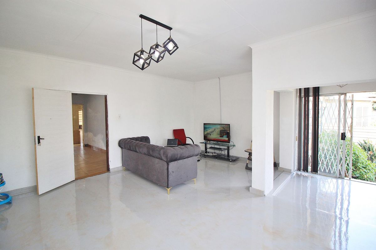 A bright living room featuring tiled flooring, modern pendant lighting, and a sliding glass door leading to the exterior.