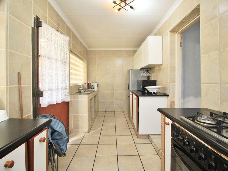 A functional kitchen featuring tiled walls and flooring, built-in cabinetry, a gas hob, and a double sink, offering a practical layout for daily use.