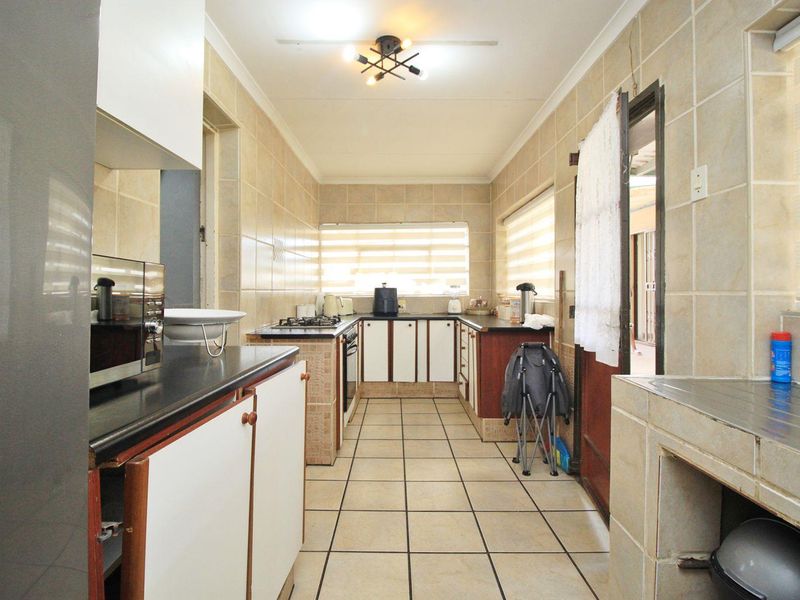 A functional kitchen featuring tiled walls and floors, built-in cabinetry, stone countertops, and a gas hob with an integrated oven.