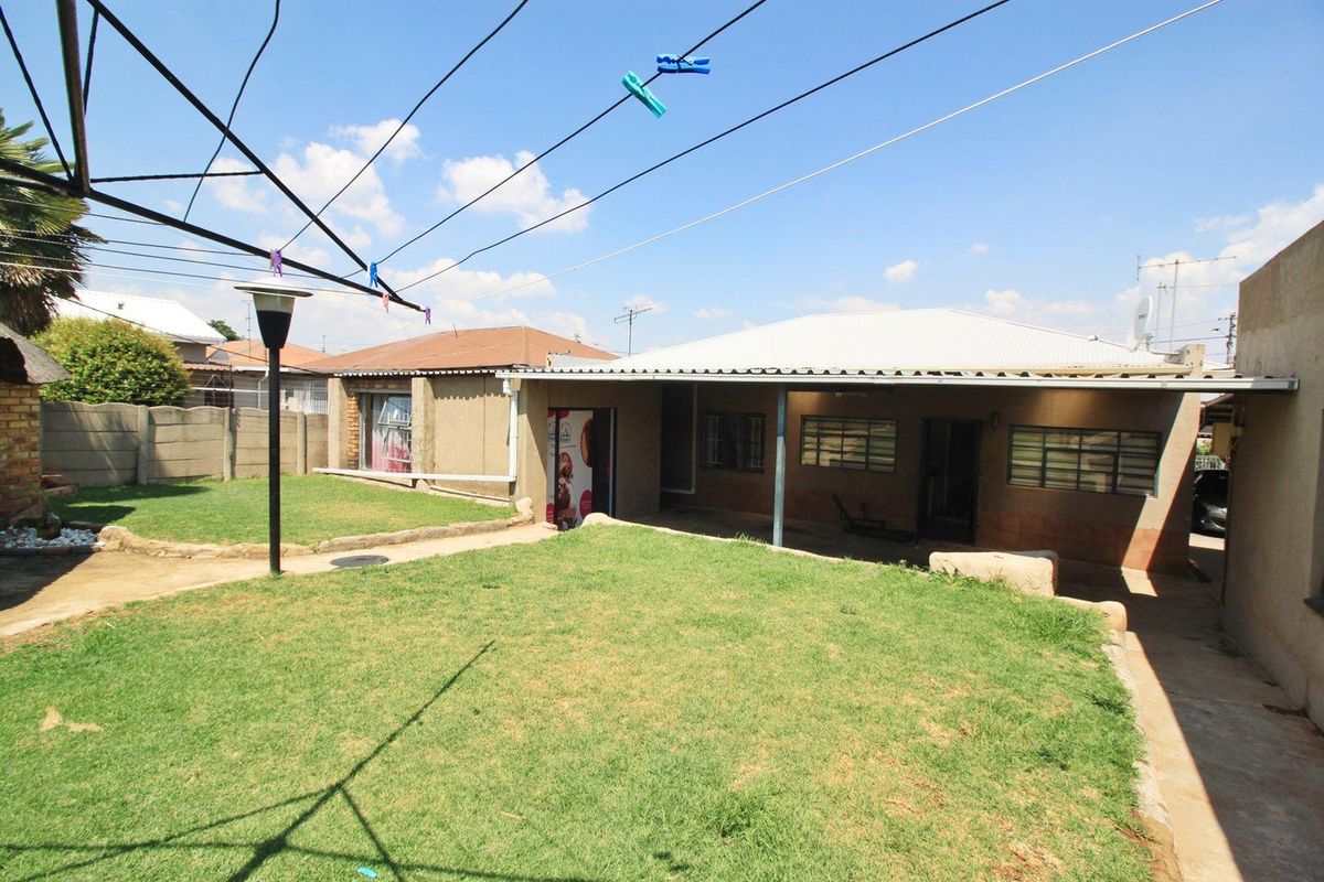 A rear view of the property featuring a covered patio area, a well-maintained lawn, and secure perimeter walling.