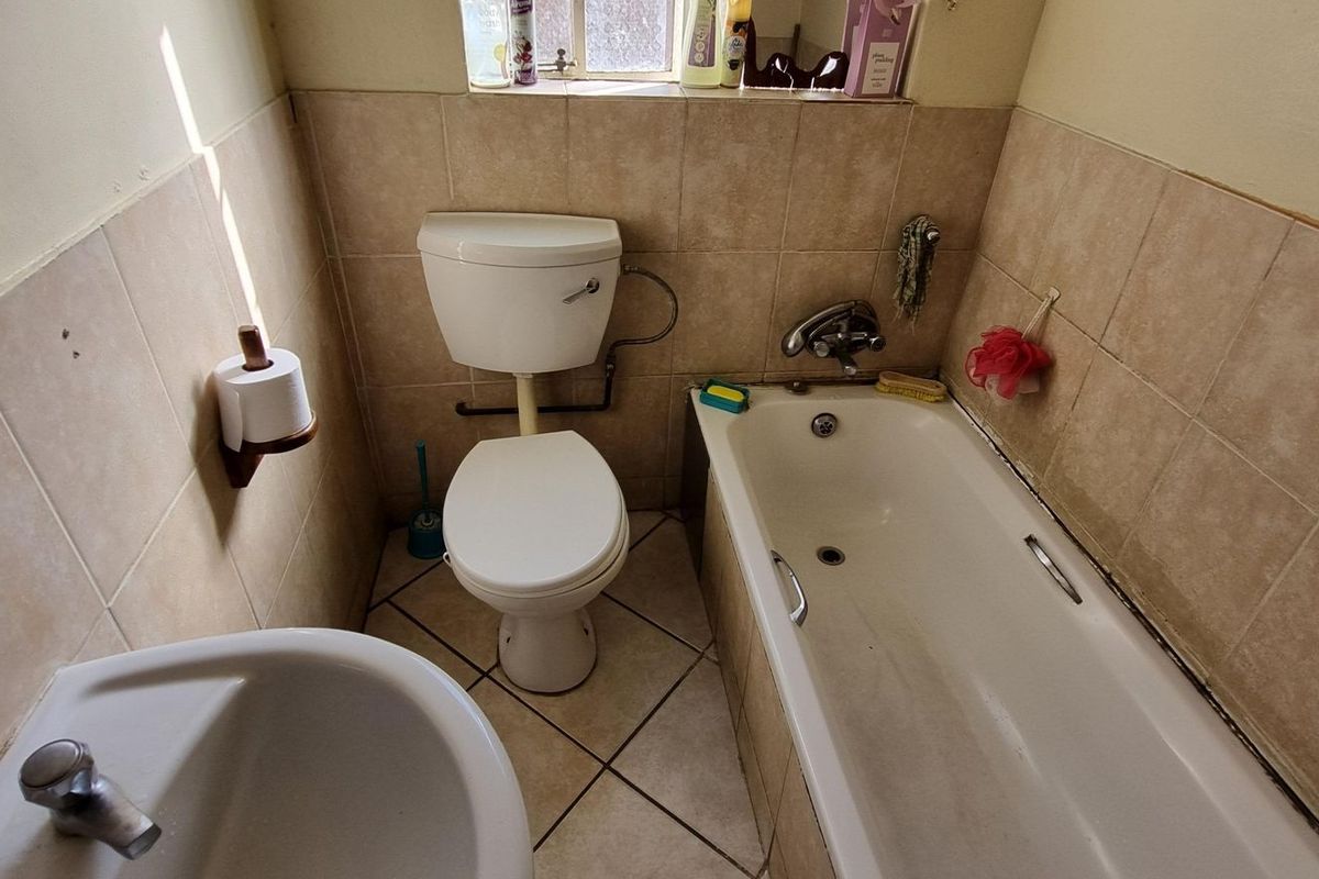 A compact bathroom featuring a standard bathtub, toilet, and pedestal basin with tiled walls and flooring.