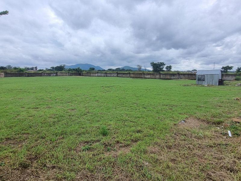 A large, open residential plot featuring a grass lawn, perimeter walling, and distant mountain views.