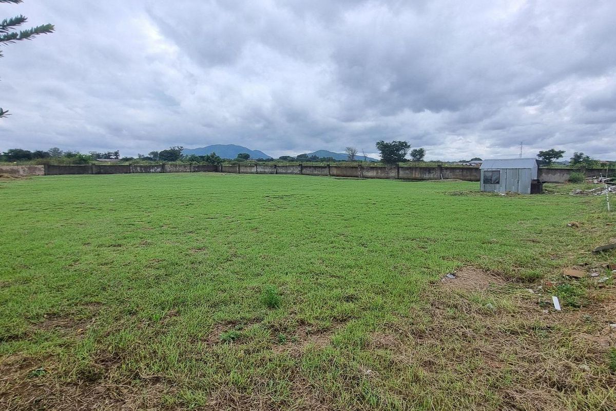 A large, open residential plot featuring a grass lawn, perimeter walling, and distant mountain views.