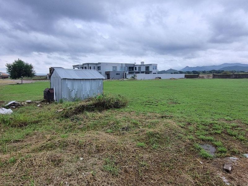 A view of a vacant residential plot featuring a metal storage shed, grass lawn, and perimeter boundary wall under an overcast sky.