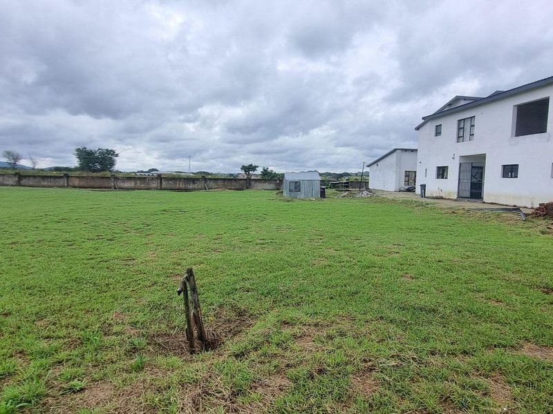 A spacious residential plot featuring a large lawn, perimeter wall, and an existing multi-story structure with an adjacent outbuilding.