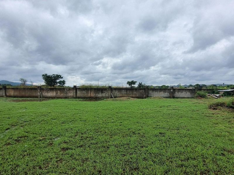 A vacant residential plot featuring a grassed area, a perimeter concrete boundary wall, and a small corrugated metal storage structure.
