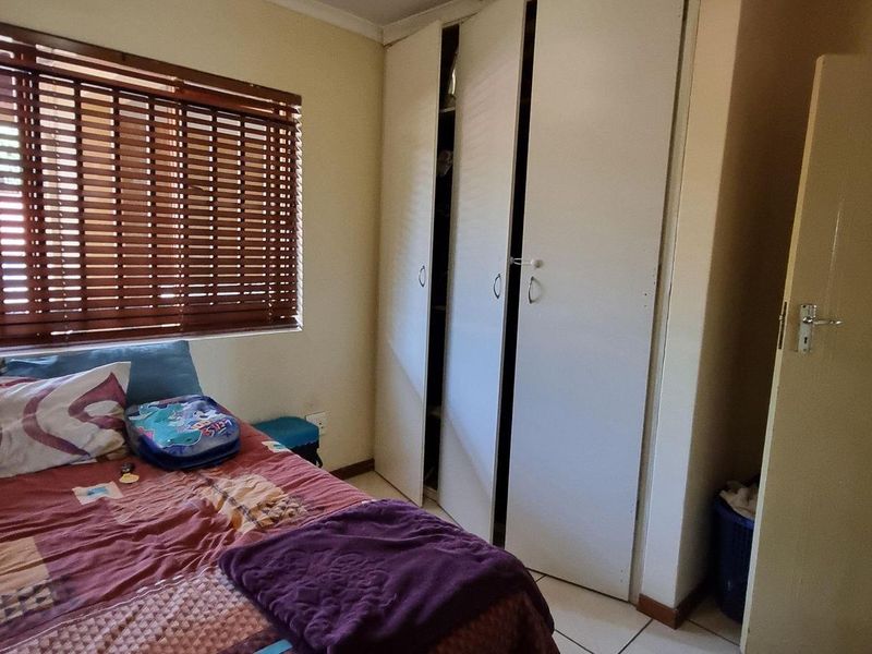 A functional bedroom featuring built-in cupboards, tiled flooring, and wooden venetian blinds, offering a practical layout for comfortable living.
