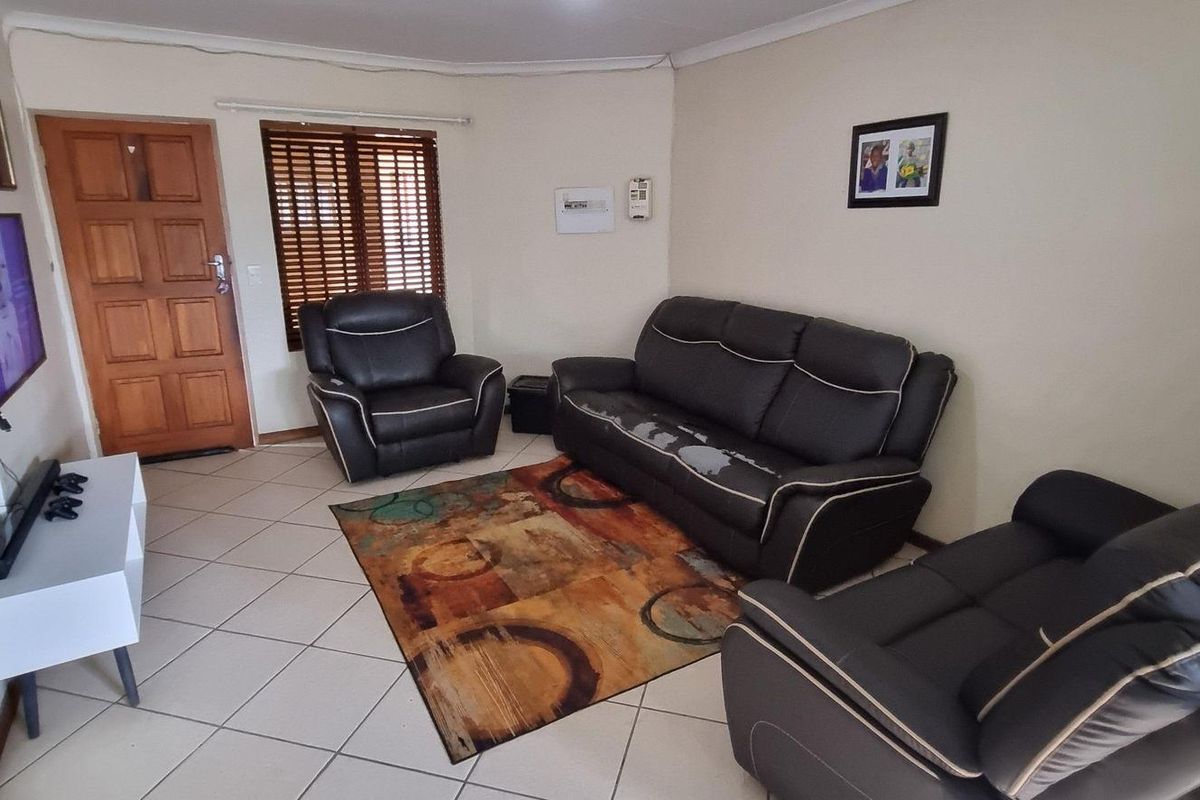 A functional living room featuring tiled flooring, a wooden entrance door, and venetian blinds, providing a neutral base for potential interior updates.