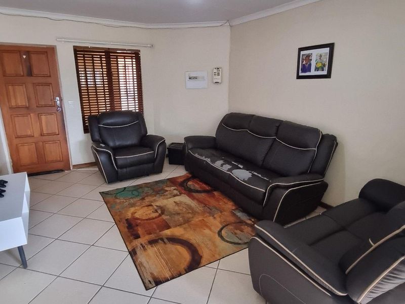 A functional living room featuring tiled flooring, a wooden entrance door, and venetian blinds, providing a neutral base for potential interior updates.