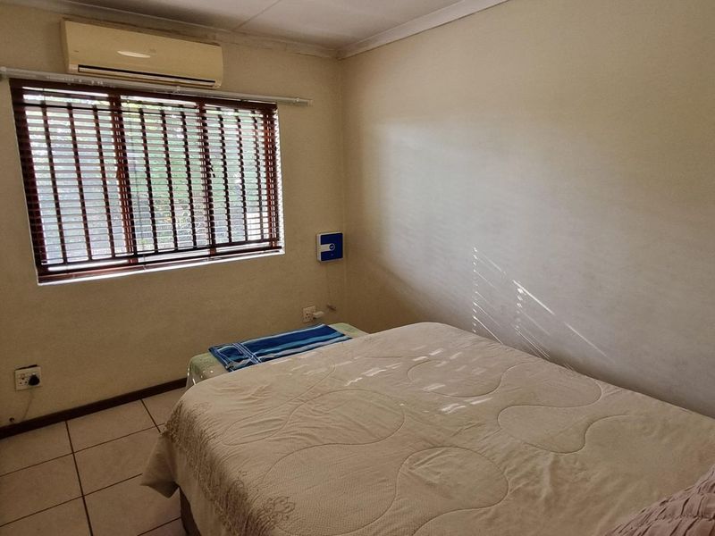 A functional bedroom featuring tiled flooring, a built-in wardrobe, and a wall-mounted air conditioning unit with venetian blinds on the window.