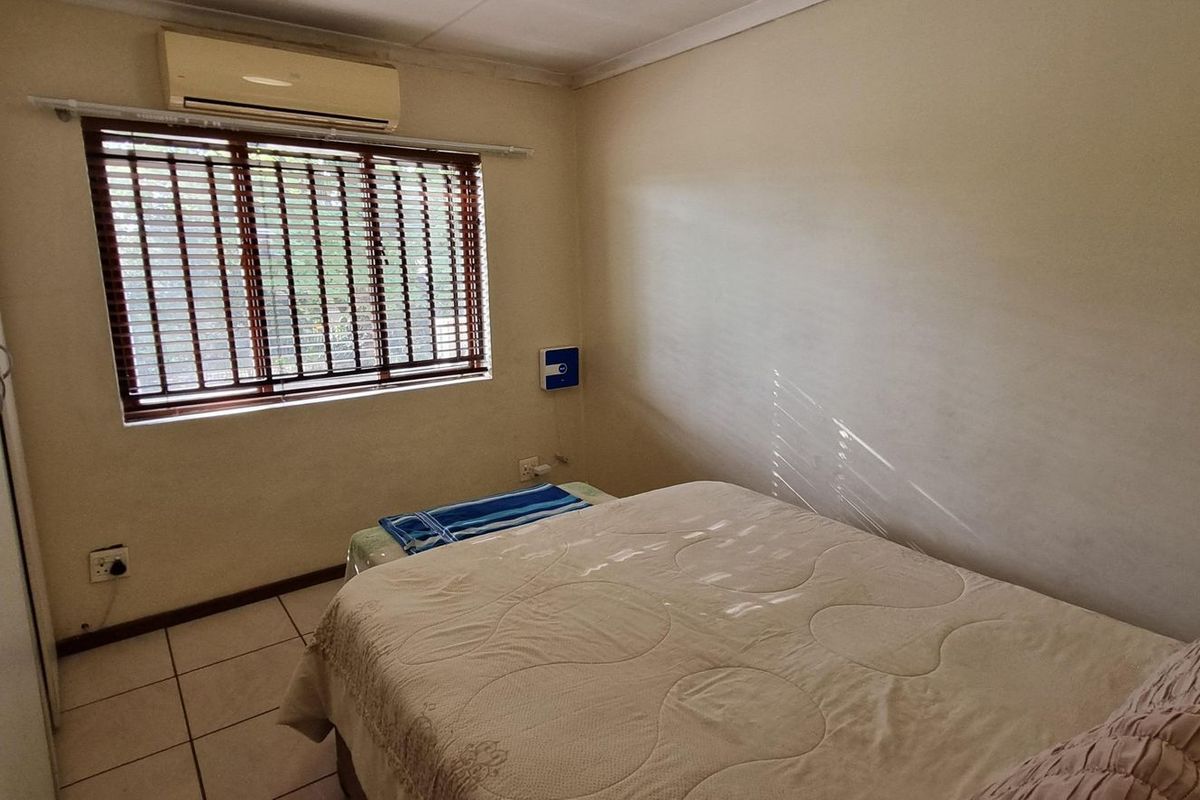 A functional bedroom featuring tiled flooring, a built-in wardrobe, and a wall-mounted air conditioning unit with venetian blinds on the window.
