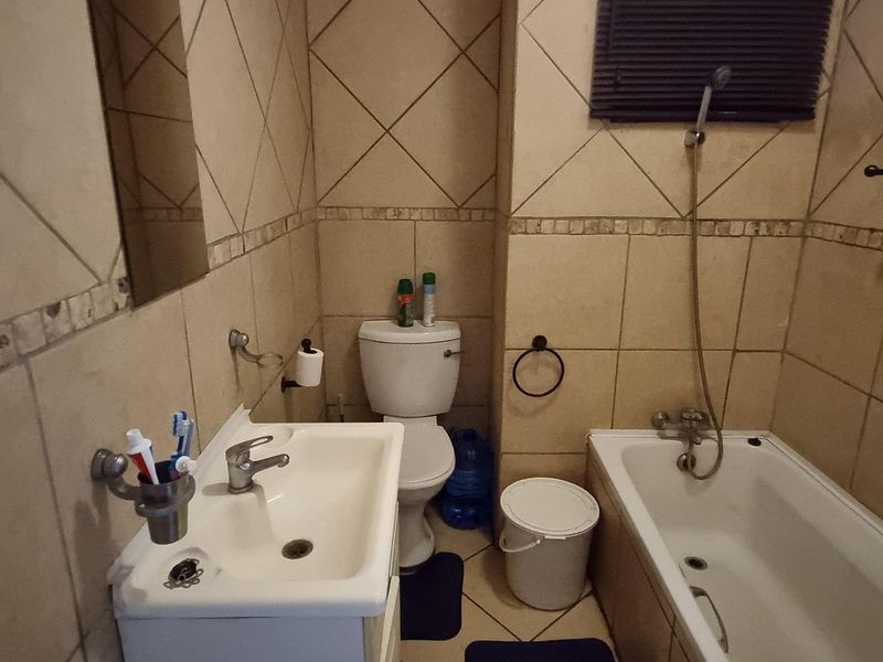 A functional bathroom featuring a pedestal basin, toilet, and a bathtub with a handheld shower mixer, finished with neutral ceramic wall and floor tiles.