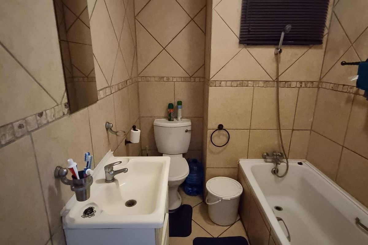A functional bathroom featuring a pedestal basin, toilet, and a bathtub with a handheld shower mixer, finished with neutral ceramic wall and floor tiles.