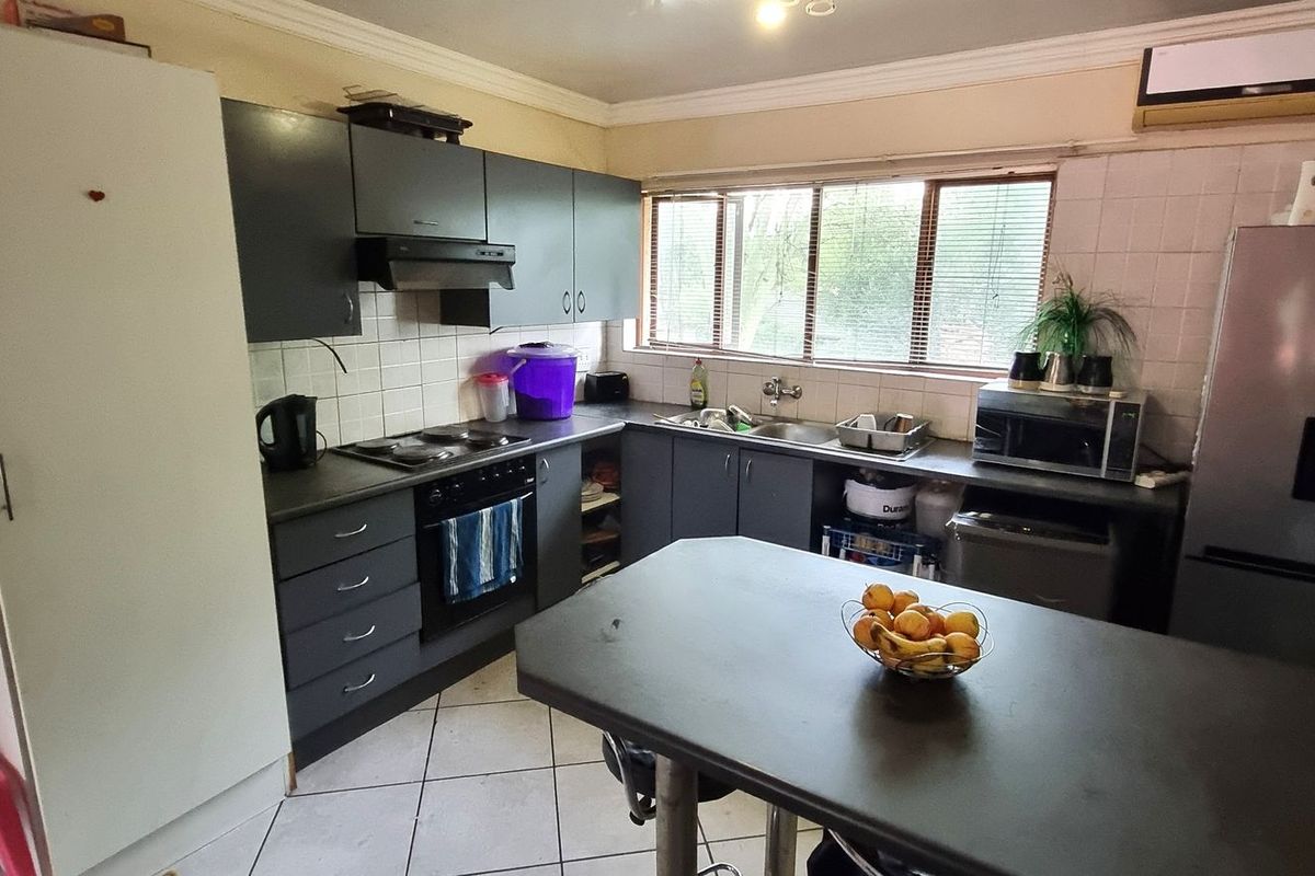 Functional kitchen featuring dark cabinetry, built-in oven and hob, tiled backsplash, and a central breakfast counter, offering a practical layout for daily use.