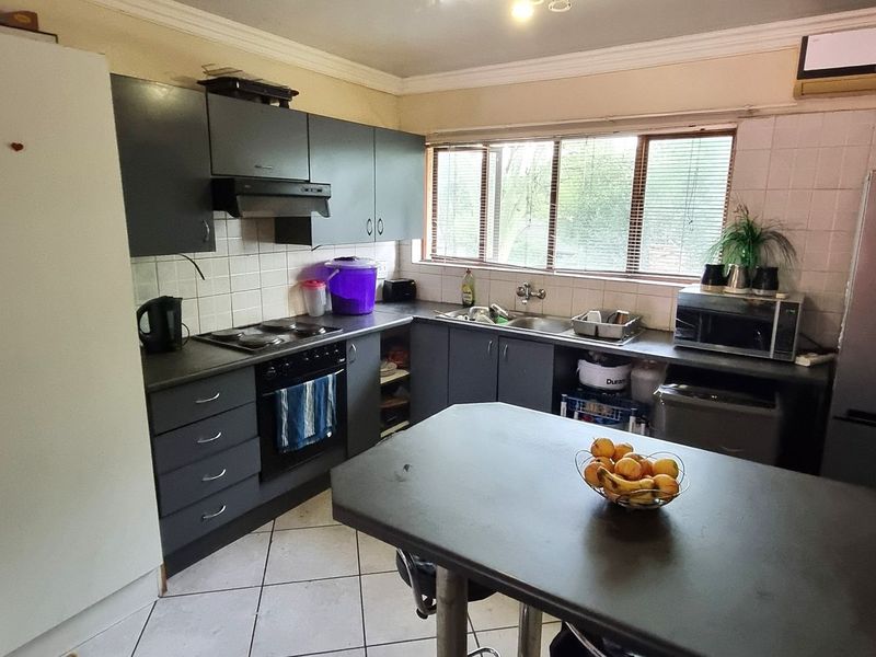 Functional kitchen featuring dark cabinetry, built-in oven and hob, tiled backsplash, and a central breakfast counter, offering a practical layout for daily use.