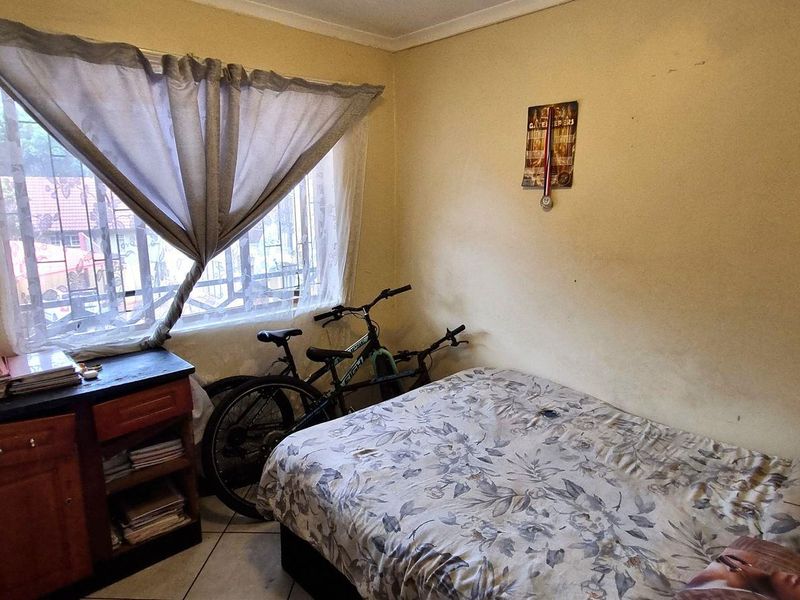 A compact bedroom featuring tiled flooring, a built-in wardrobe, and a window fitted with security bars.
