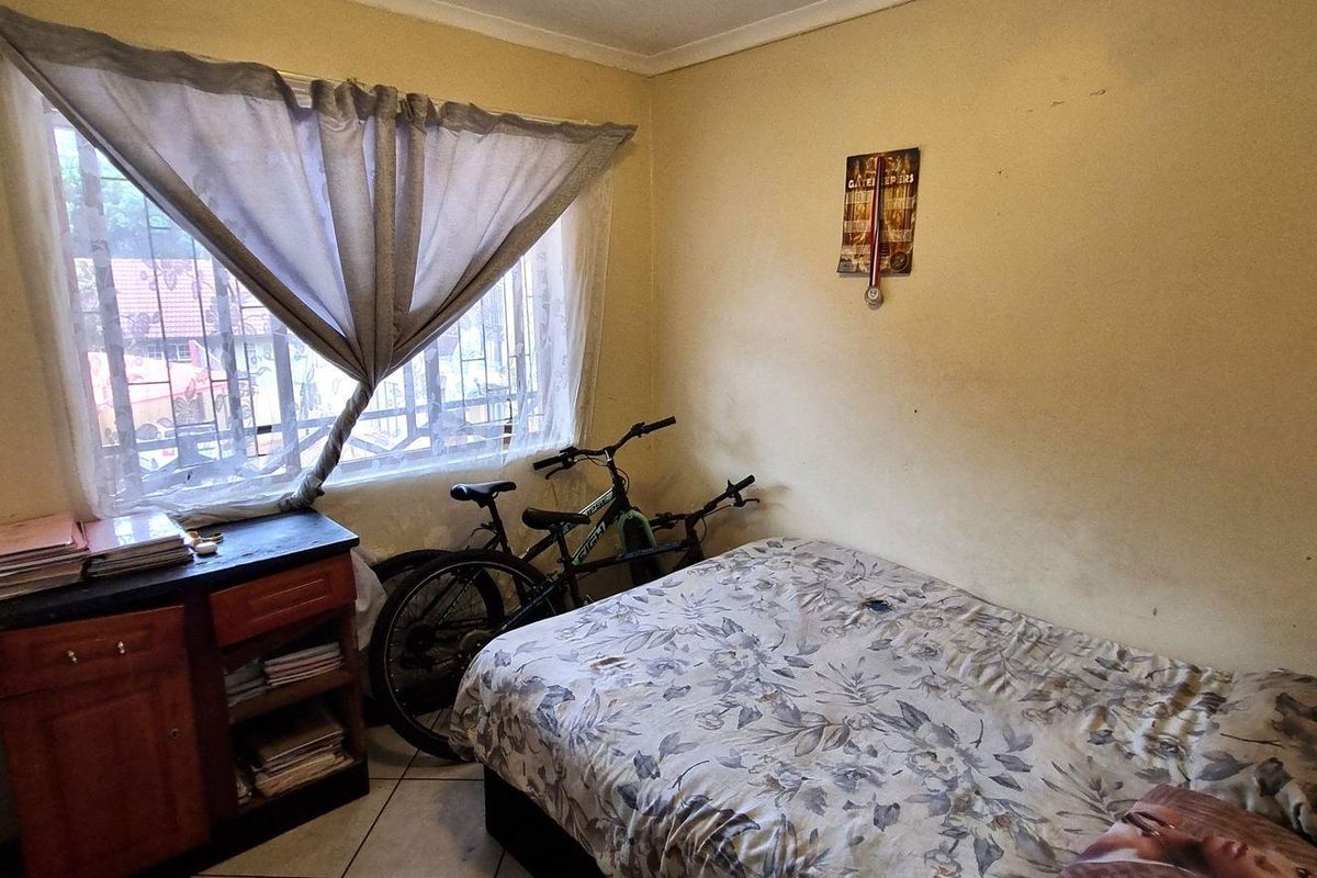 A compact bedroom featuring tiled flooring, a built-in wardrobe, and a window fitted with security bars.