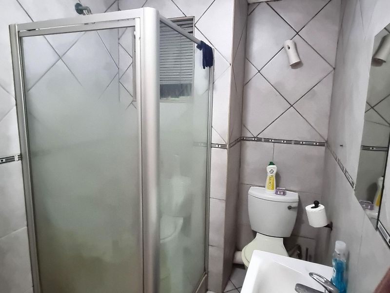 A compact bathroom featuring a shower enclosure, toilet, and washbasin with tiled walls and flooring.