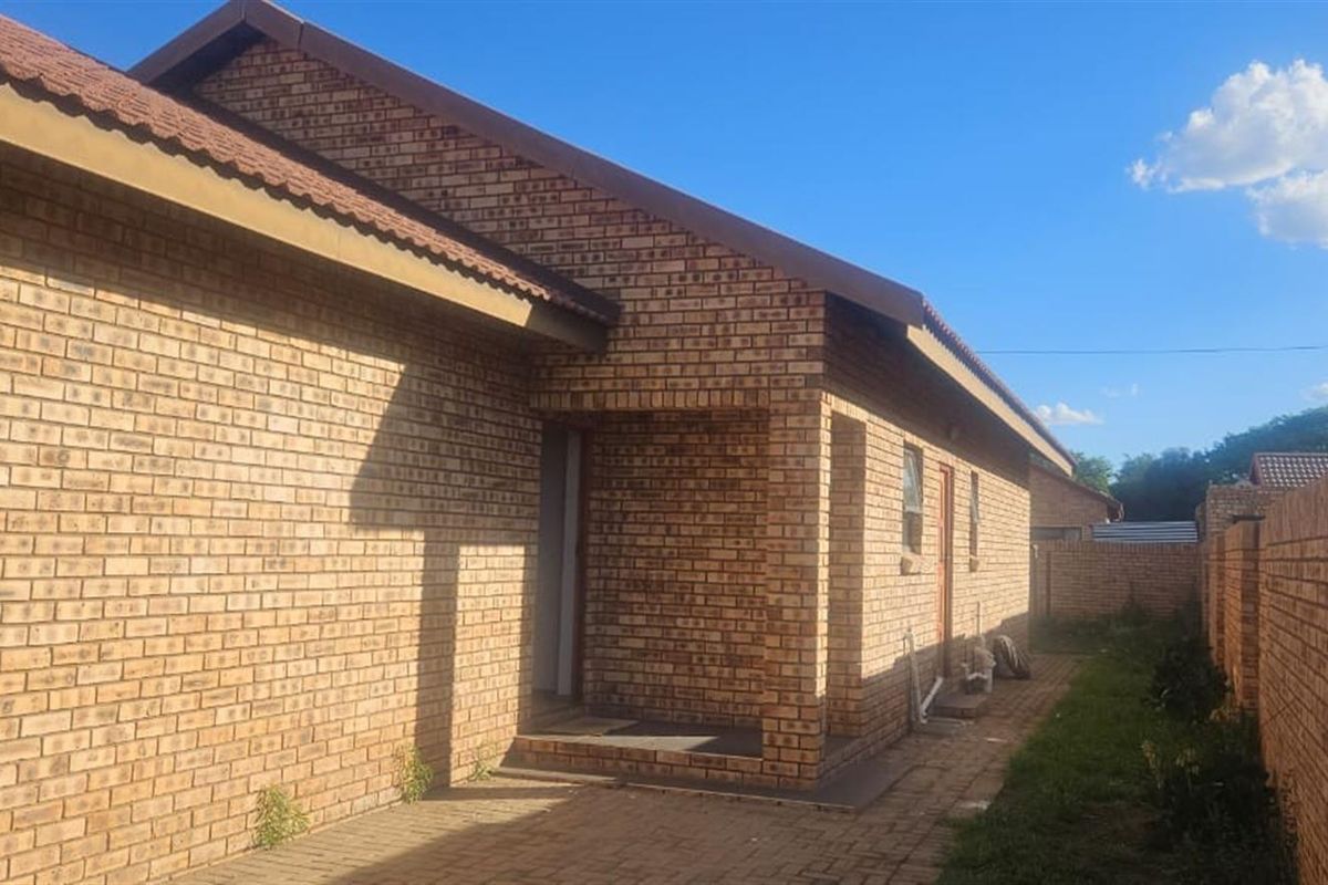 A view of the rear exterior of the face brick house, featuring a paved walkway and a surrounding boundary wall.