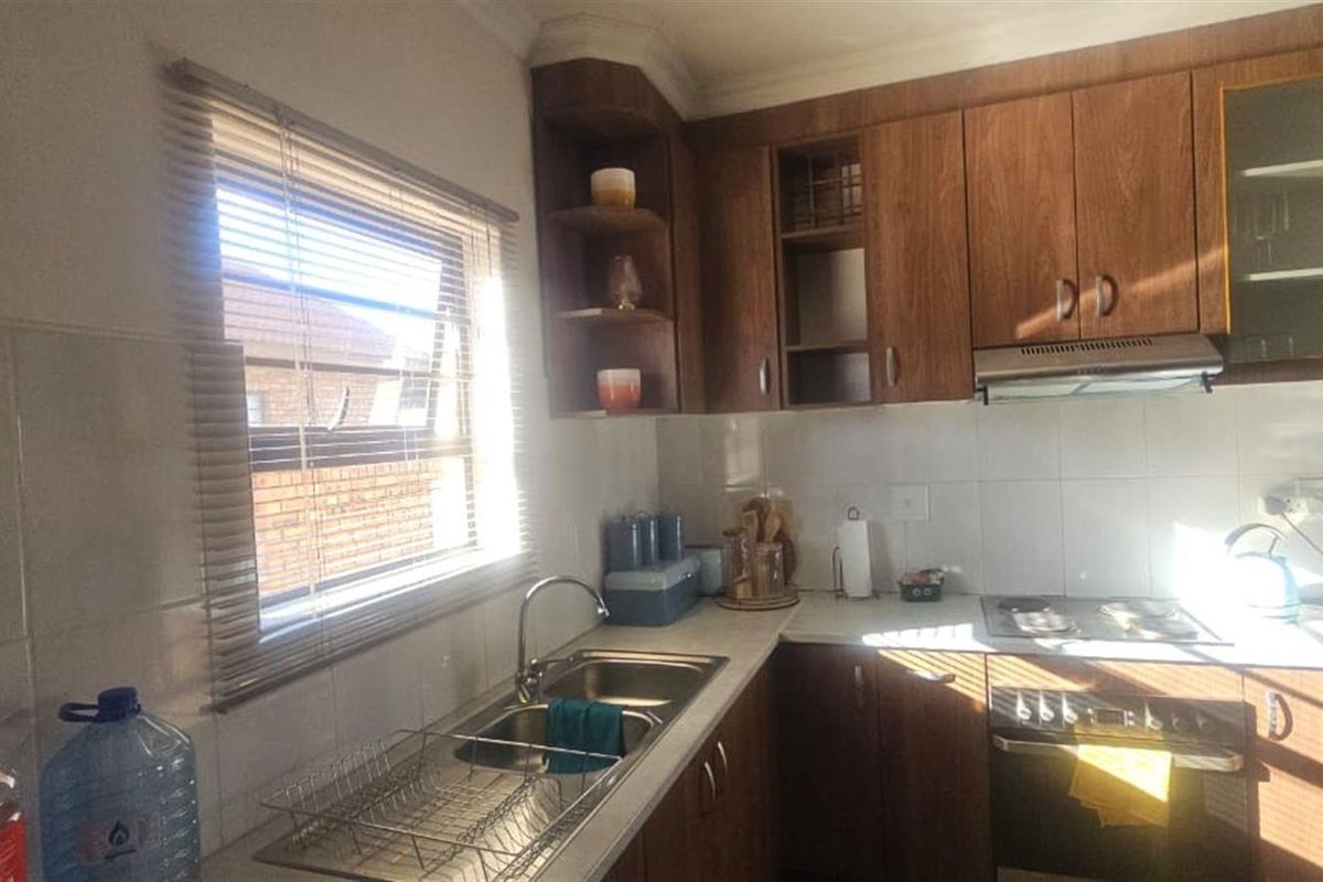 A functional kitchen featuring wooden cabinetry, a stainless steel sink, built-in oven, electric hob, and tiled splashback, offering a classic layout.